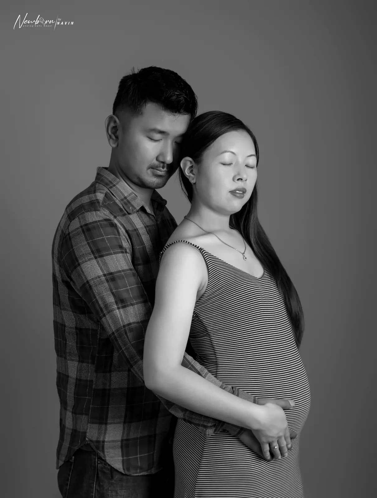 Expecting parents in a black and white portrait, the father resting his head against the mother's, her hands on her bump.