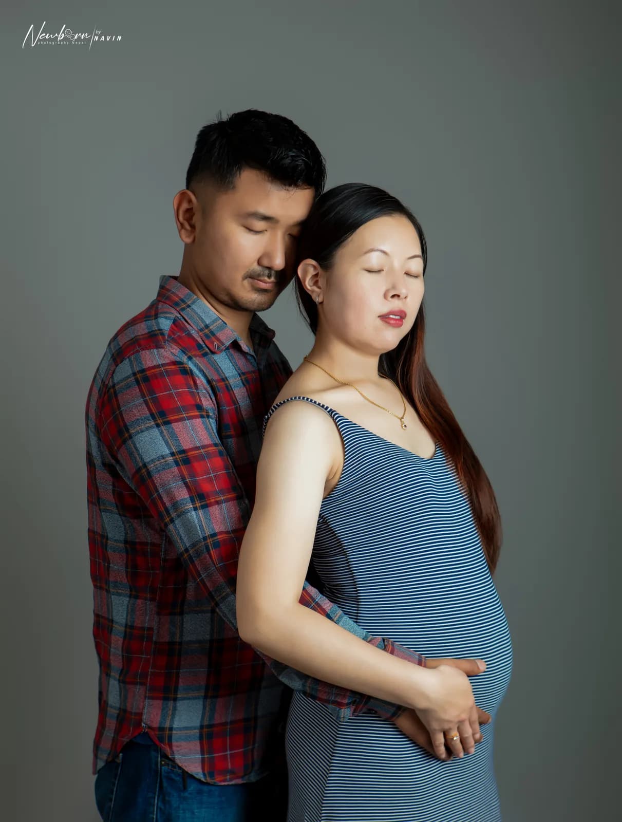 Expecting parents in a black and white close portrait, both with eyes closed, the mother's hands on her bump.