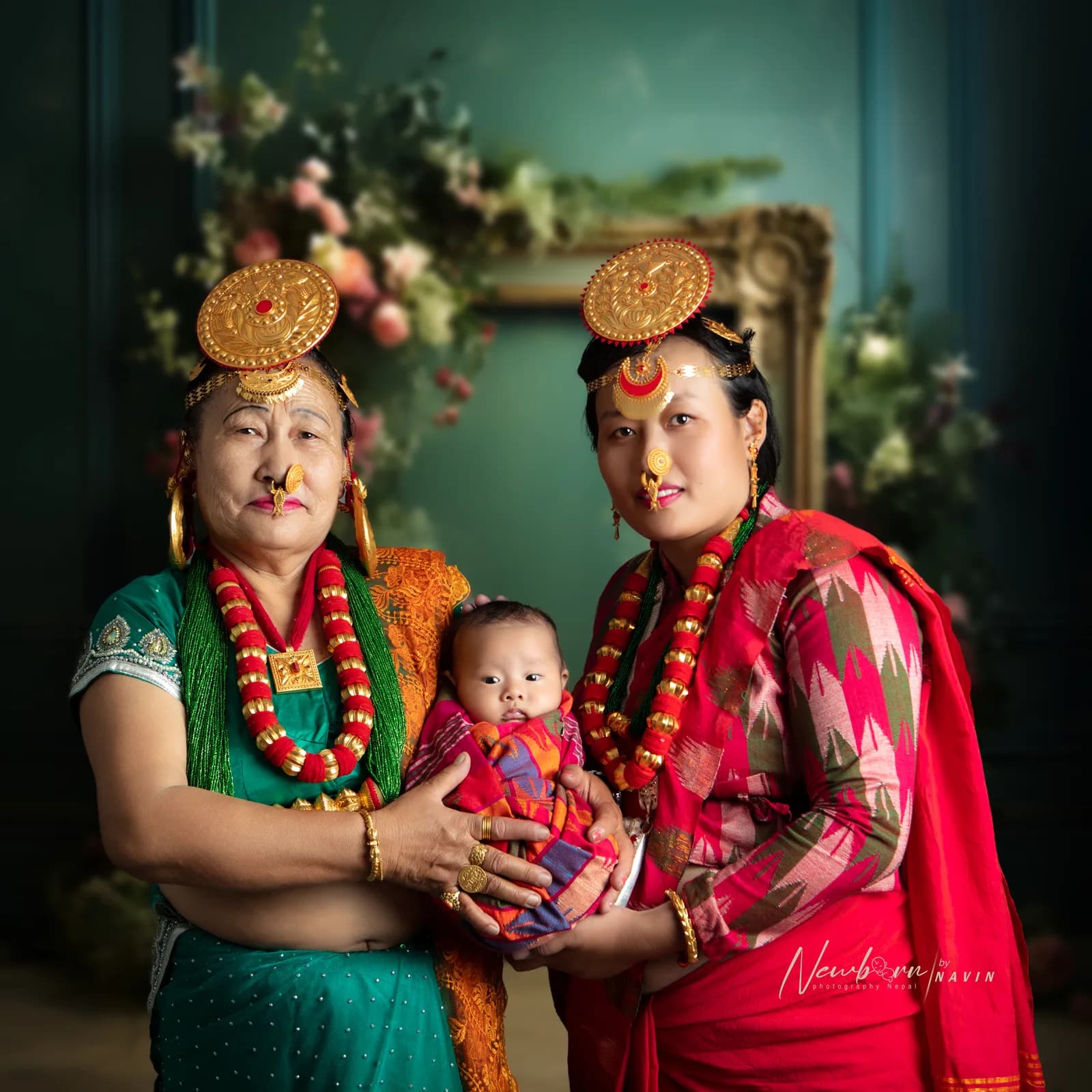 Grandmother, mother and newborn baby dressed in traditional Nepali gold jewelry and clothing, a three-generation family portrait with a floral backdrop.
