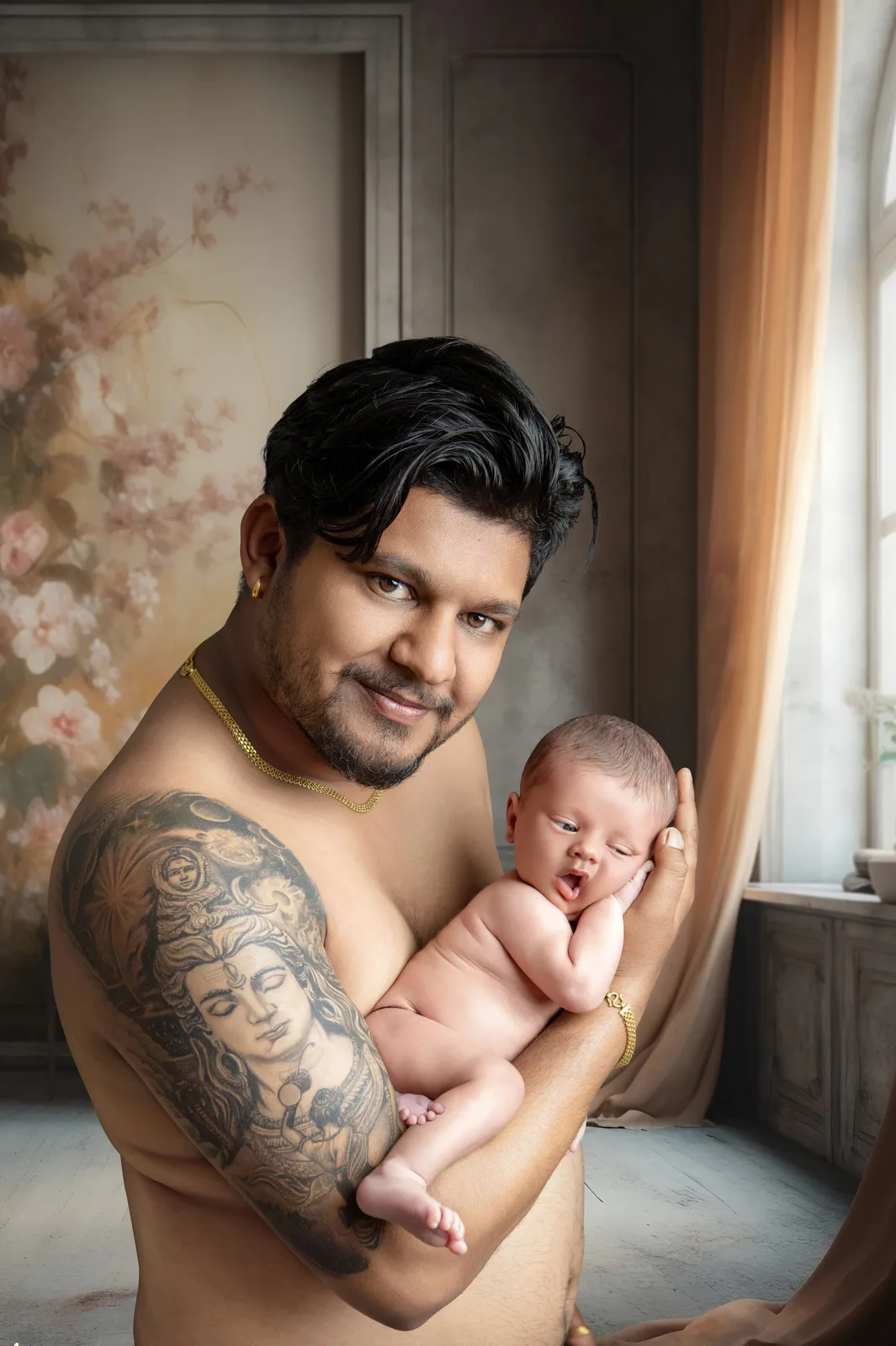 Mother in a pink sweater holding her newborn baby, who wears a pink outfit, beside a window with sheer curtains and a potted palm.